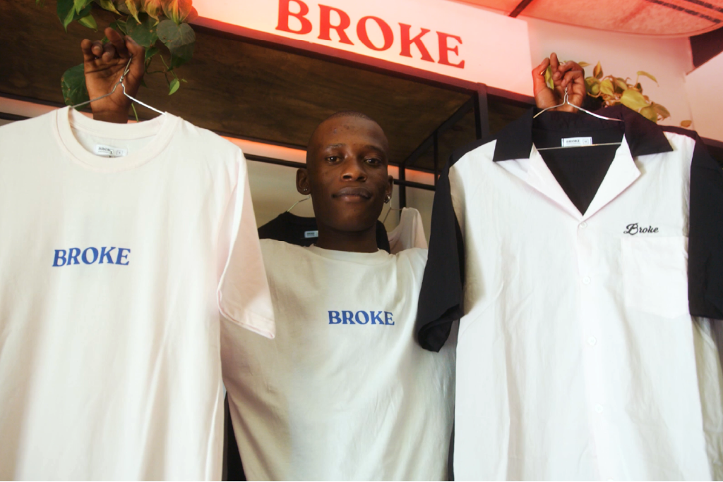 Andile Dlamini founder of BROKE holding up tshirts
